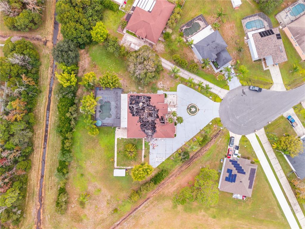 An aerial view shows a residential property with a house featuring a severely fire-damaged roof — 214 TARANTO WAY, KISSIMMEE, FL