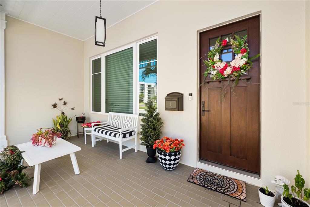 A covered front porch features a wooden door, a white bench, and potted plants — 1 PALM TERRACE, BELLEAIR, FL