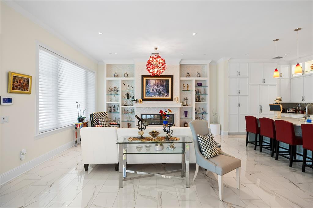 An open-concept living room and kitchen featuring white cabinetry, marble-look tile flooring, and a fireplace — 1 PALM TERRACE, BELLEAIR, FL