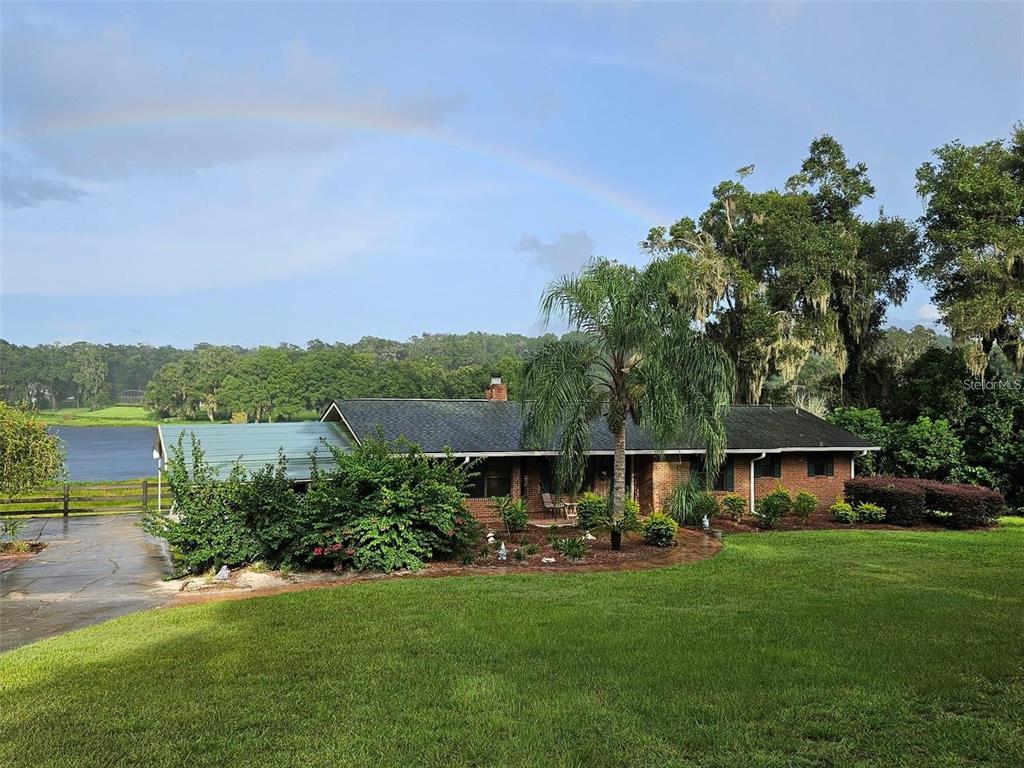 A brick house with a dark shingled roof sits on a lawn beside a lake — 2285 WILMHURST ROAD, DELAND, FL