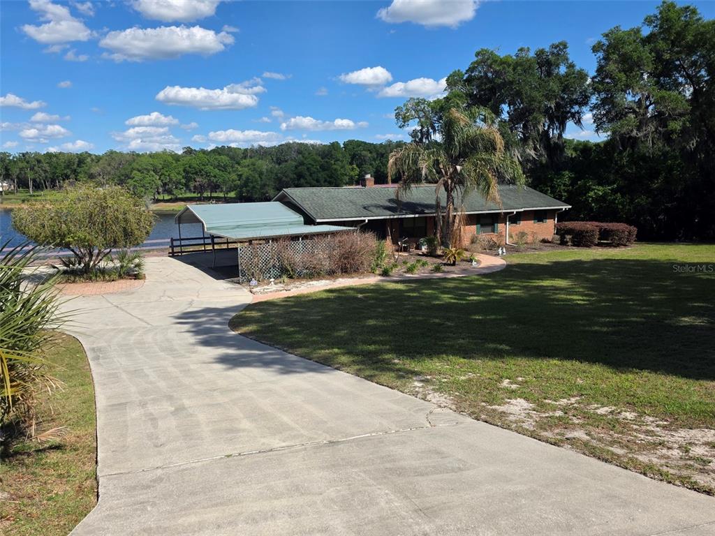 A single-story brick house with a metal carport sits on a grassy lot near water — 2285 WILMHURST ROAD, DELAND, FL