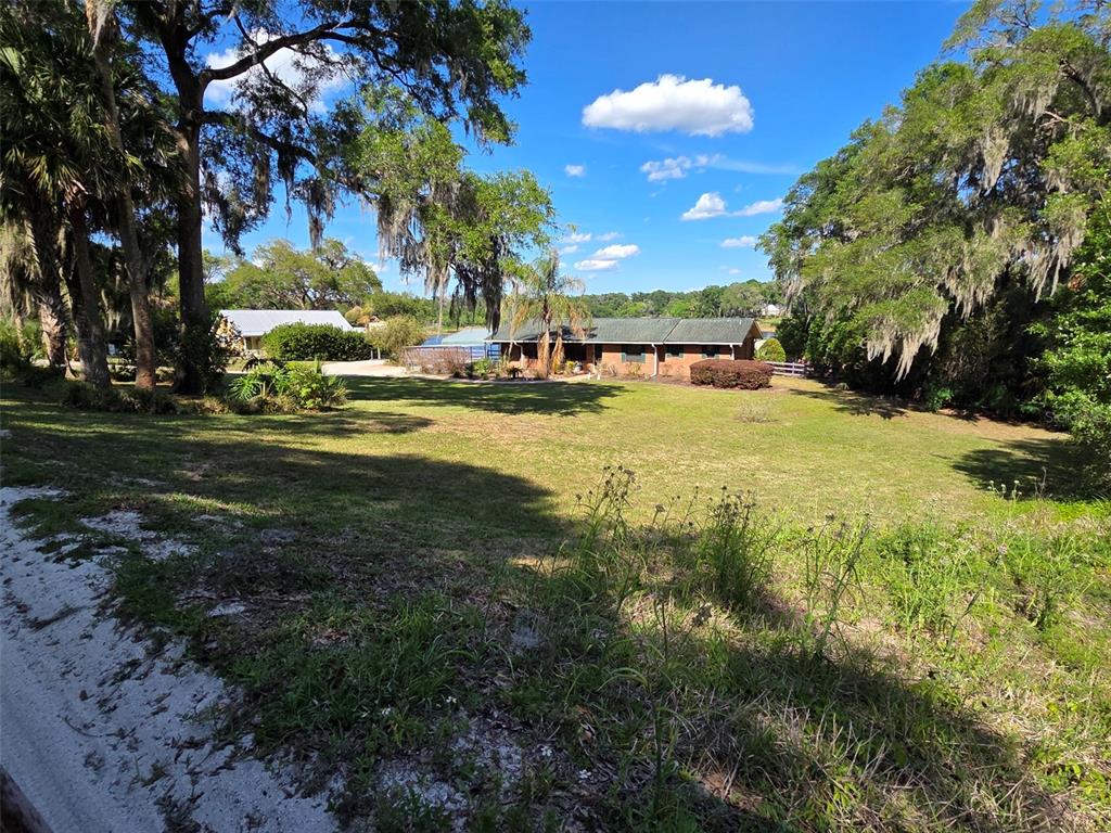 A single-story brick house sits on a large grassy lot surrounded by mature trees — 2285 WILMHURST ROAD, DELAND, FL