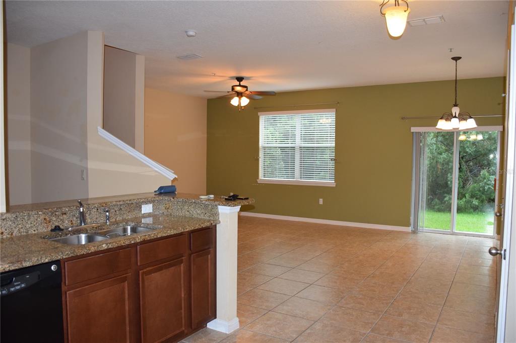 A kitchen with granite countertops overlooks an open living area with tile floors and sliding doors — 1516 SCARLET OAK LOOP UNIT B, WINTER GARDEN, FL