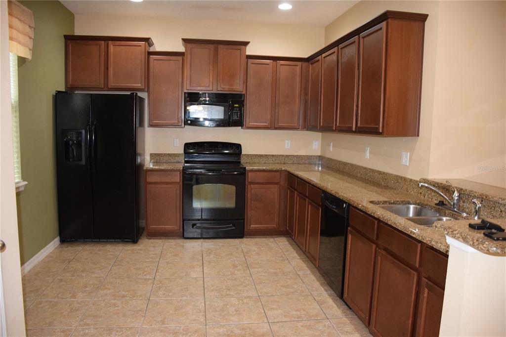 A kitchen features dark wood cabinets, granite countertops, black appliances, and light-colored tile flooring — 1516 SCARLET OAK LOOP UNIT B, WINTER GARDEN, FL