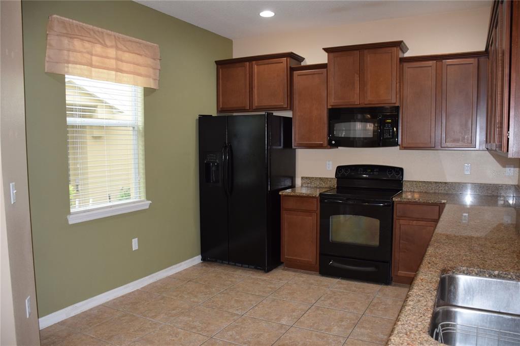 A kitchen features brown cabinets, black appliances, granite countertops, and a window with a valance — 1516 SCARLET OAK LOOP UNIT B, WINTER GARDEN, FL