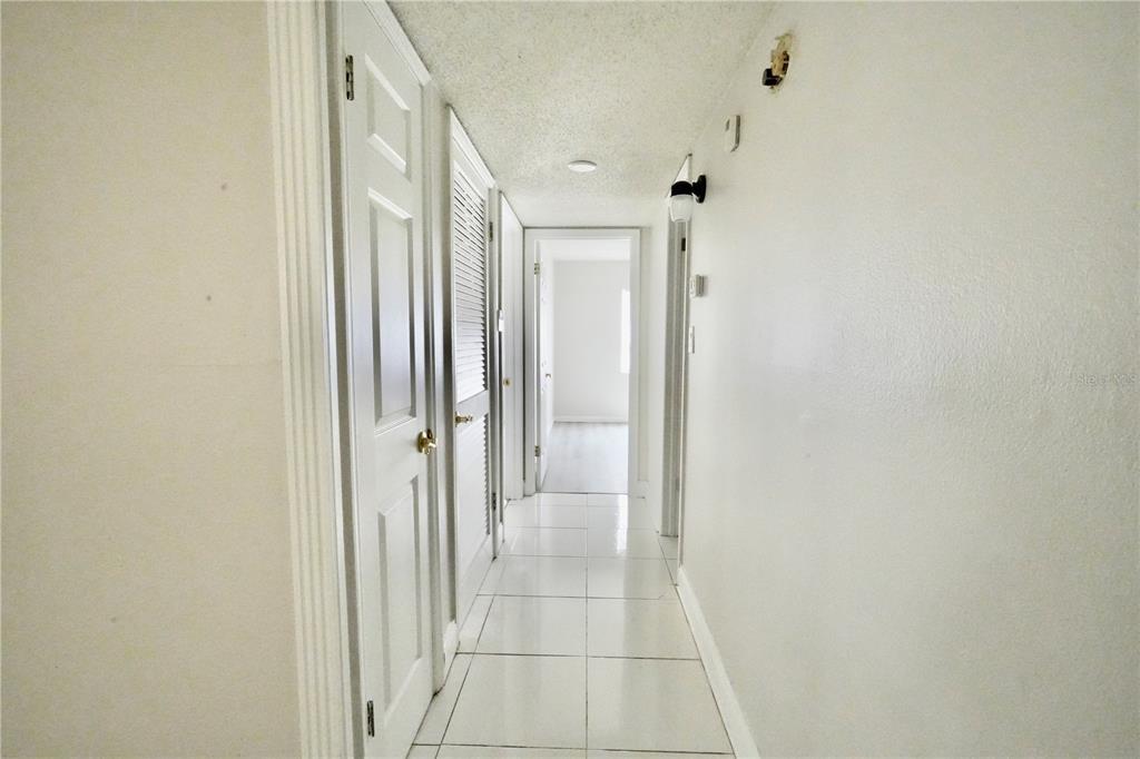 A white hallway with tiled flooring leads to a doorway at the end — 4718 CHRISTA COURT UNIT 317, TAMPA, FL