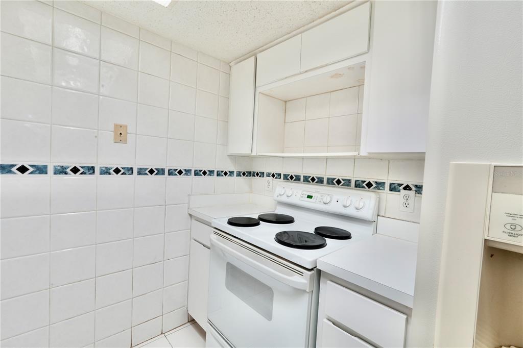 A kitchen features white tiled walls, white cabinets, and a white electric stove — 4718 CHRISTA COURT UNIT 317, TAMPA, FL
