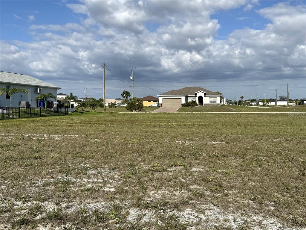 A large, vacant grassy lot sits in front of a suburban house under a cloudy sky — 3436 NW 45TH AVENUE, CAPE CORAL, FL