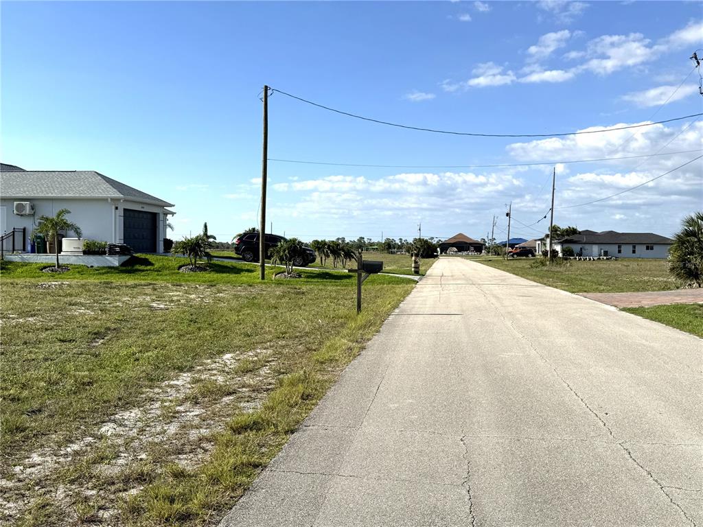 A paved road runs between residential lots with houses and utility poles under a blue sky — 3436 NW 45TH AVENUE, CAPE CORAL, FL