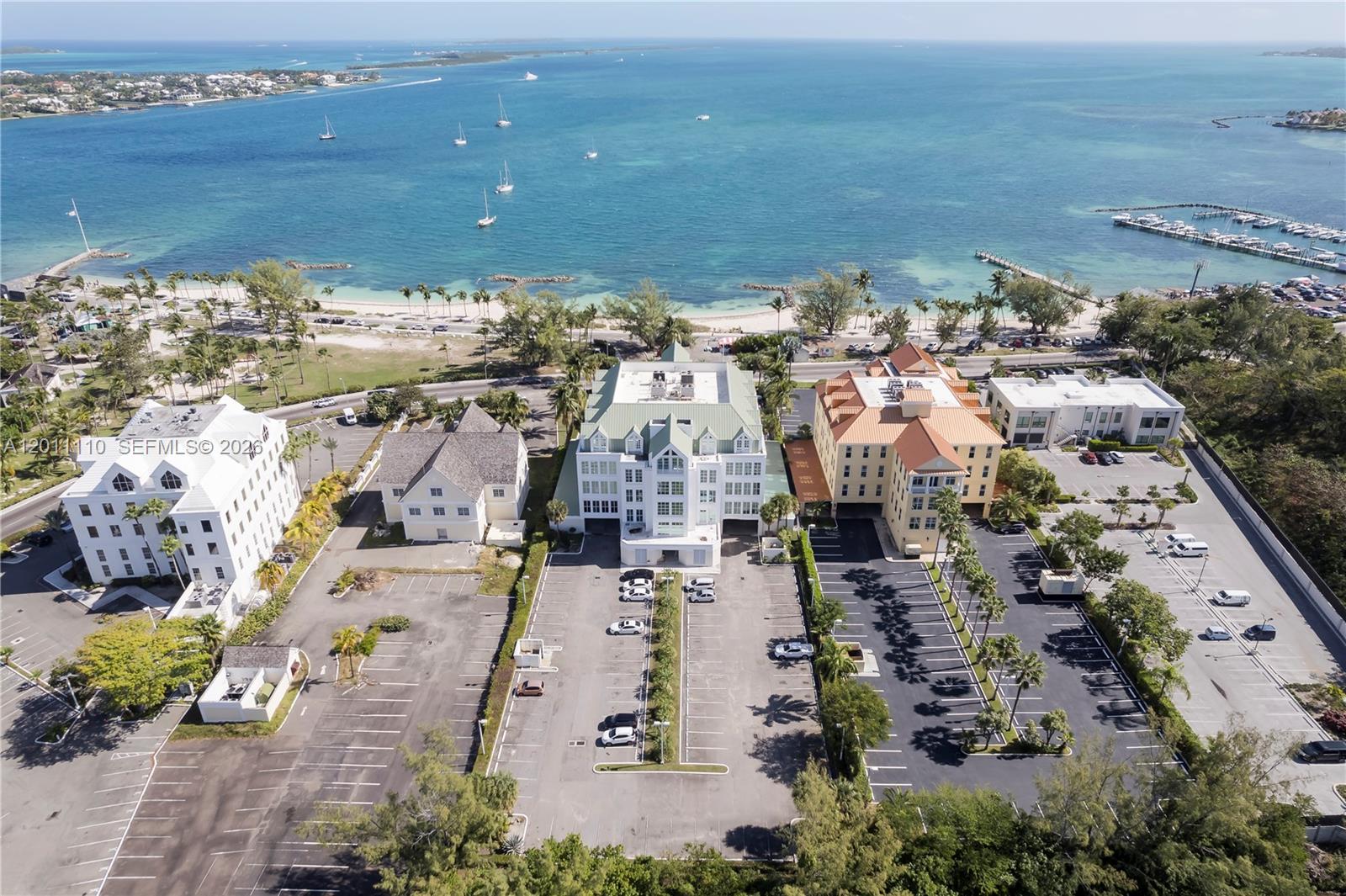 An aerial view shows three multi-story buildings with parking lots situated near a coastal beach — 9 E Bay Street, 00000, FL