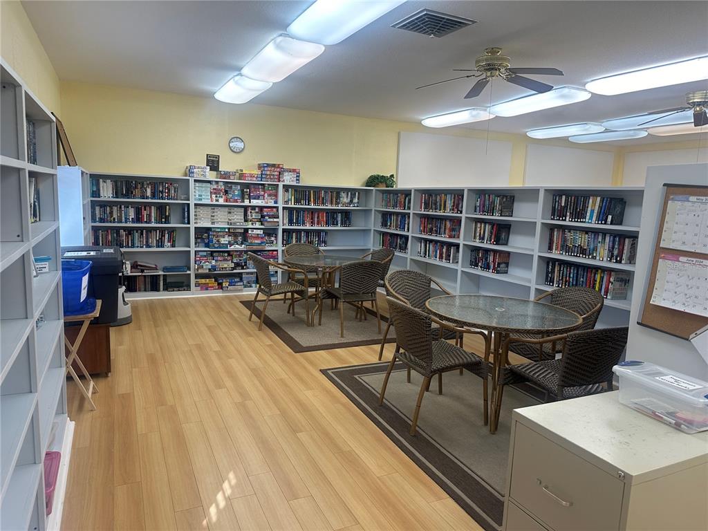 A library room features light wood flooring, multiple bookshelves, and two small tables with chairs — 5621 SUNFLOWER ROAD, VENICE, FL