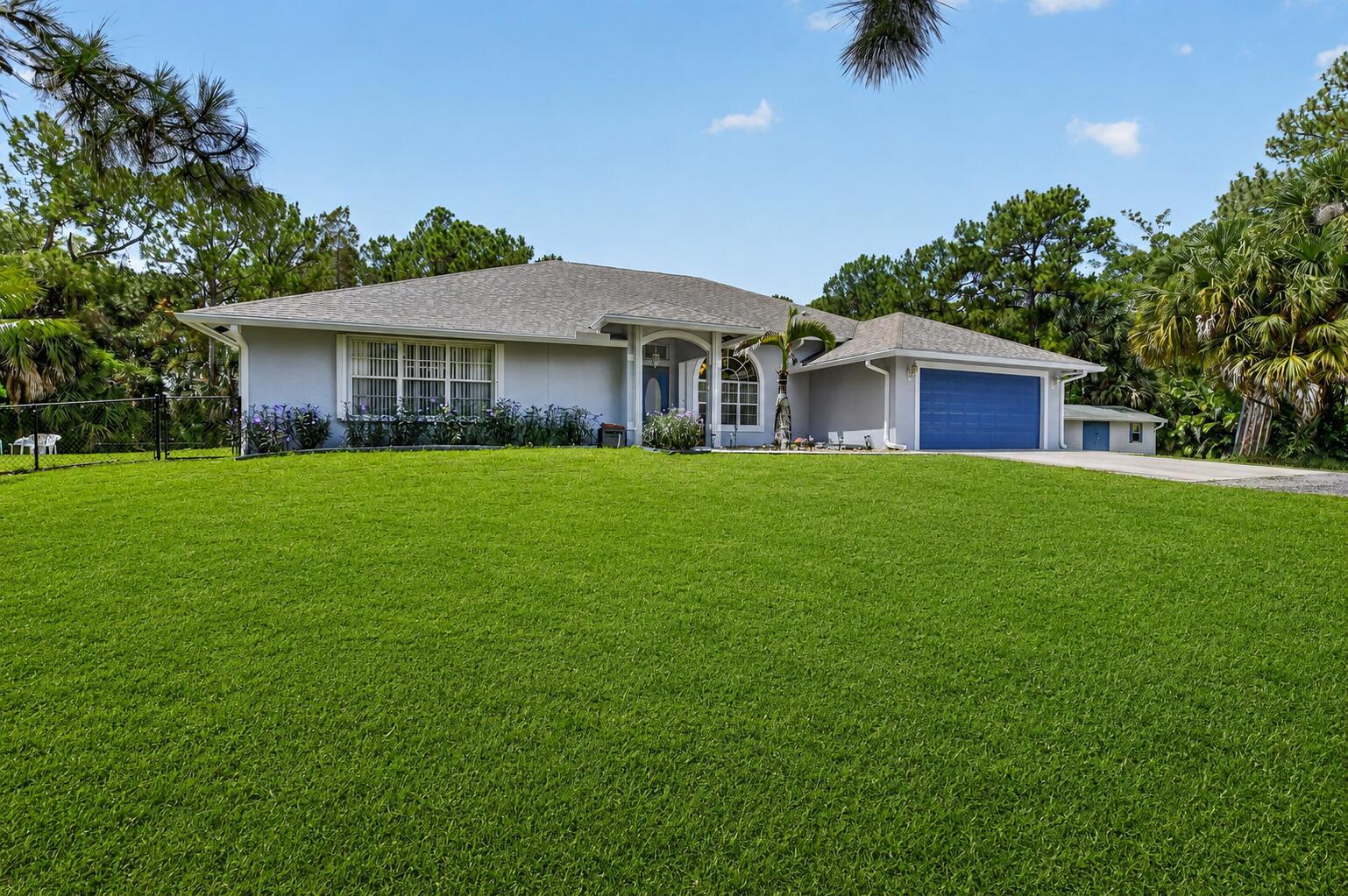 A single-story house with a grey exterior, blue garage door, and a large front lawn — 16074 66th Court N, FL 33470, FL