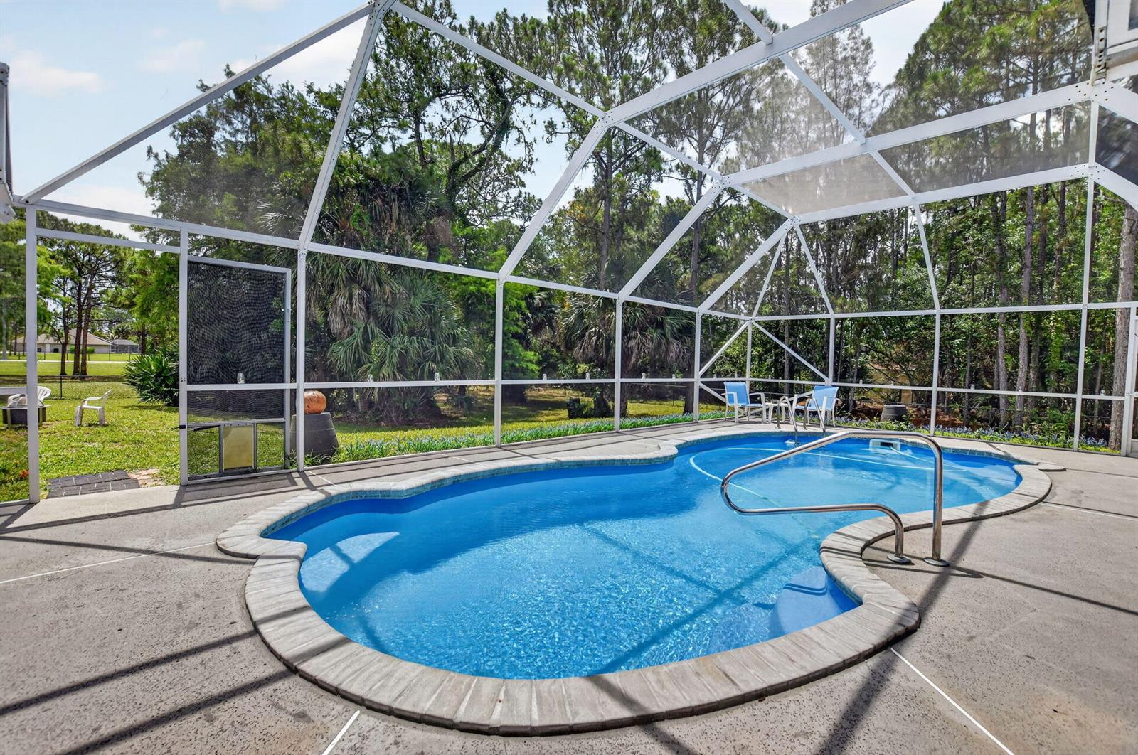 A screened-in swimming pool with a concrete deck sits in a backyard with mature trees — 16074 66th Court N, FL 33470, FL