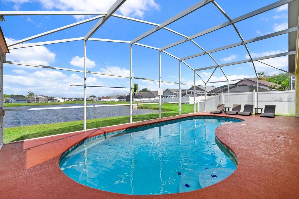 A screened-in swimming pool with a red deck overlooks a lake and neighboring houses — 5134 VIOLET LANE, KISSIMMEE, FL