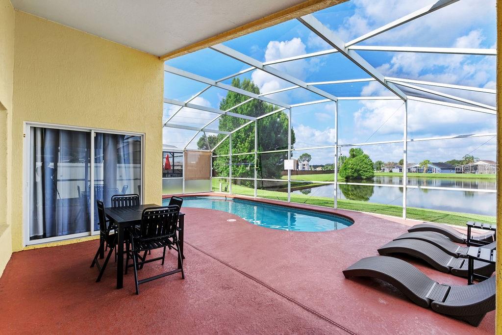 A covered patio features a swimming pool, outdoor dining set, and lounge chairs overlooking water — 5134 VIOLET LANE, KISSIMMEE, FL