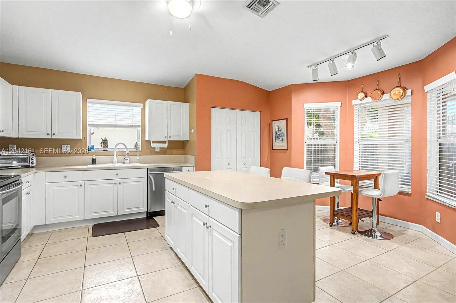 A kitchen features white cabinetry, a central island, and orange walls with tile flooring — 14033 SW 155th Ct, Miami FL 33196, MIAMI, FL