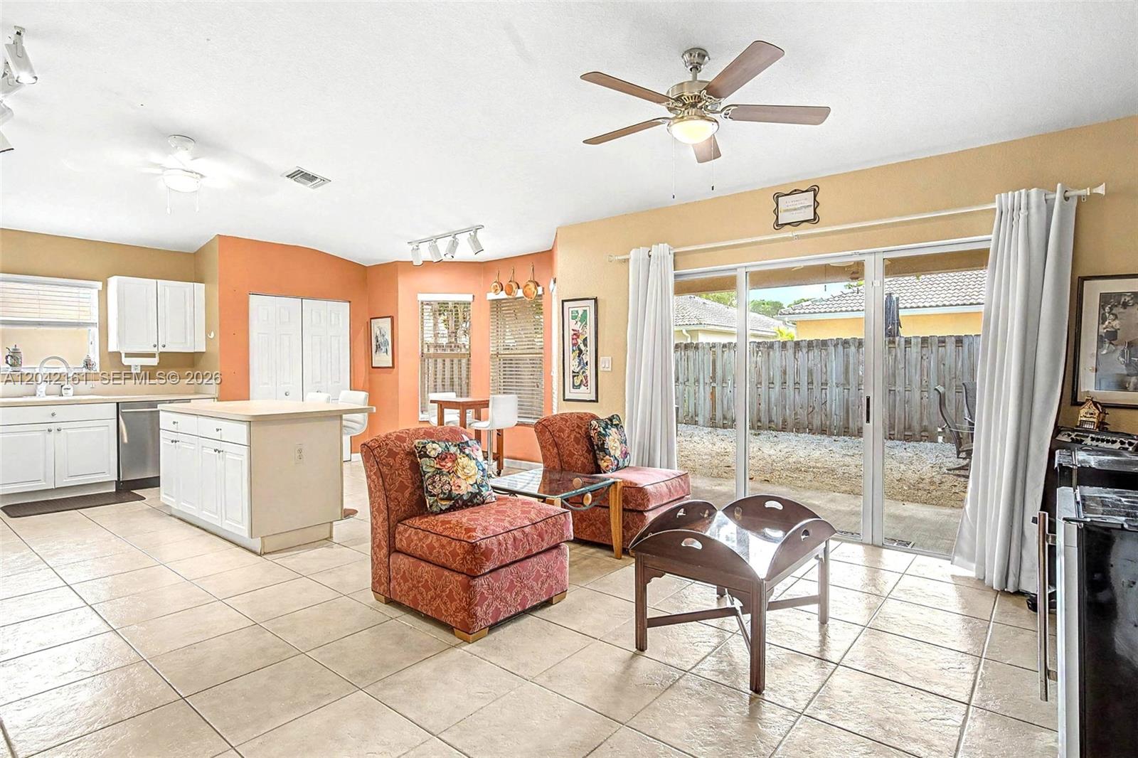 An open-concept living and kitchen area features tile flooring, white cabinetry, and sliding glass doors — 14033 SW 155th Ct, Miami FL 33196, MIAMI, FL