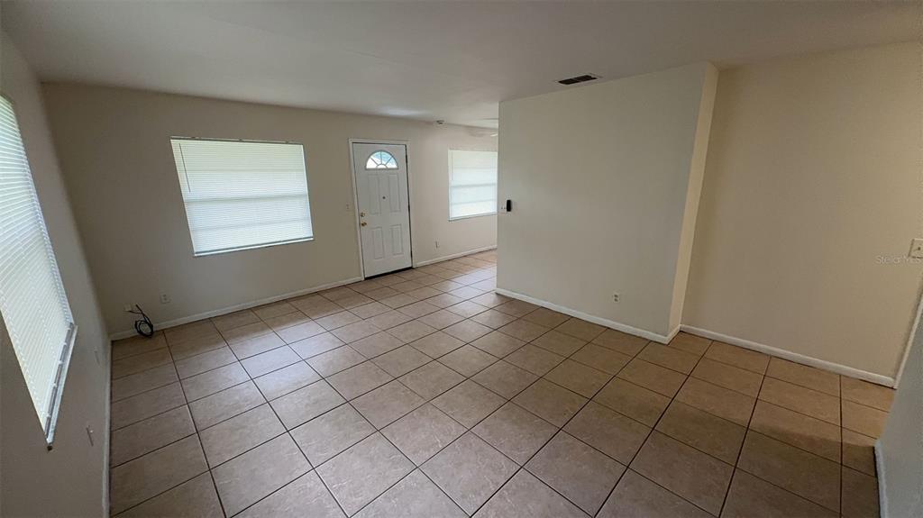 A living room with beige tile flooring, white walls, and a white front door — 4734 20TH STREET, ZEPHYRHILLS, FL