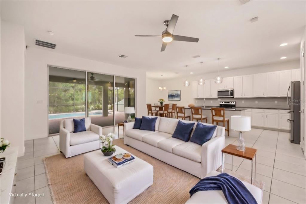A living room with white furniture and blue pillows opens to a kitchen and pool area — 1078 CASTLEVECCHIO LOOP, ORLANDO, FL