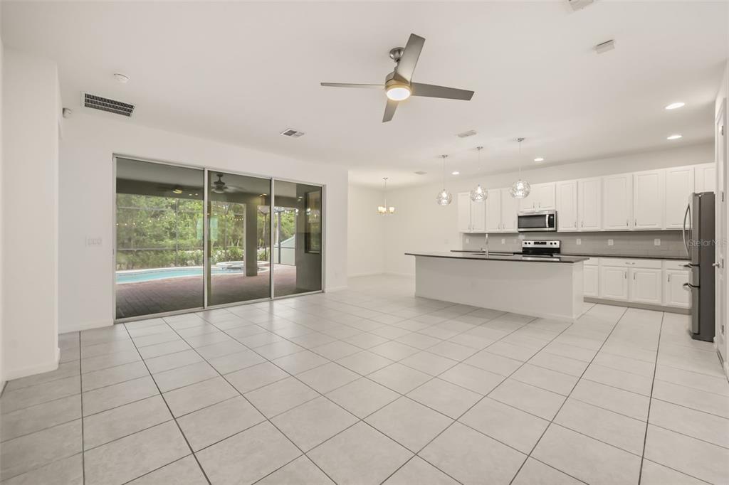 An open-concept kitchen and living area with white cabinets, a kitchen island, and sliding doors — 1078 CASTLEVECCHIO LOOP, ORLANDO, FL