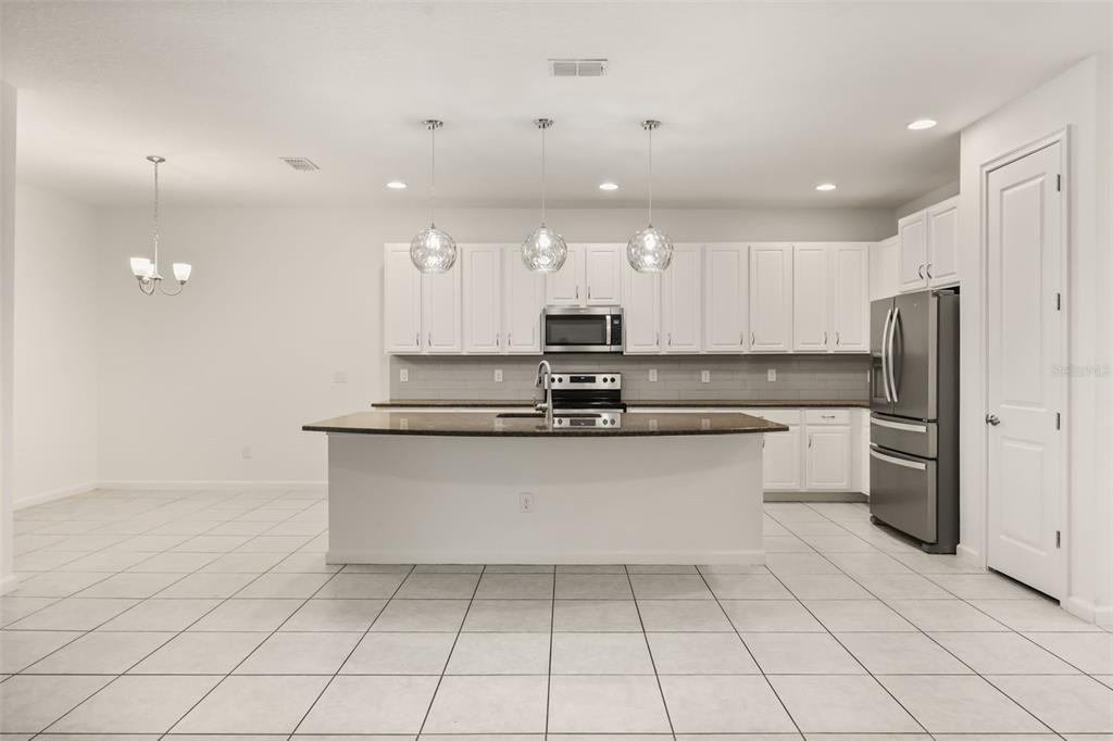 A kitchen features white cabinets, a dark granite island, stainless steel appliances, and tile flooring — 1078 CASTLEVECCHIO LOOP, ORLANDO, FL