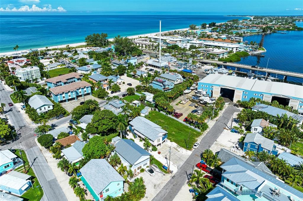 An aerial view shows a coastal neighborhood with houses, a marina, and a bridge — 204 BAY DRIVE N, BRADENTON BEACH, FL