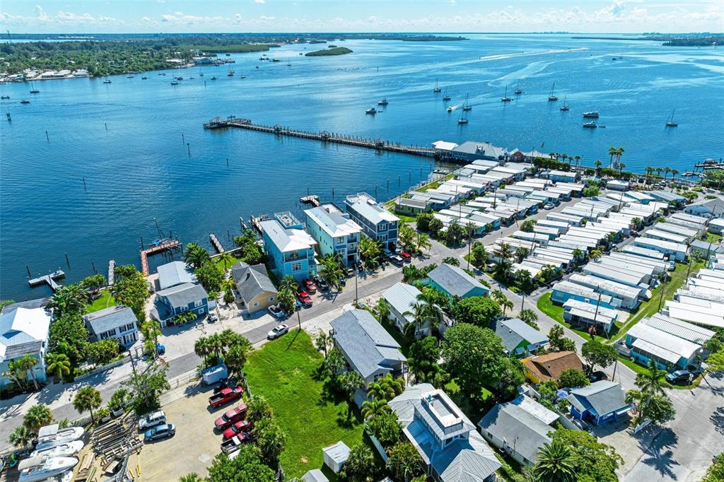 An aerial view shows a coastal neighborhood with houses, a mobile home park, and a pier — 204 BAY DRIVE N, BRADENTON BEACH, FL