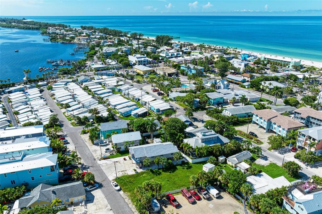 An aerial view shows a coastal neighborhood with mobile homes, houses, and a nearby beach — 204 BAY DRIVE N, BRADENTON BEACH, FL