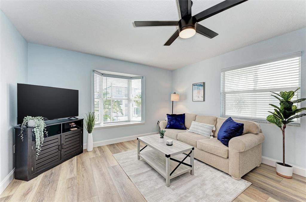 A living room features light blue walls, wood-look flooring, a beige sofa, and a television — 204 BAY DRIVE N, BRADENTON BEACH, FL