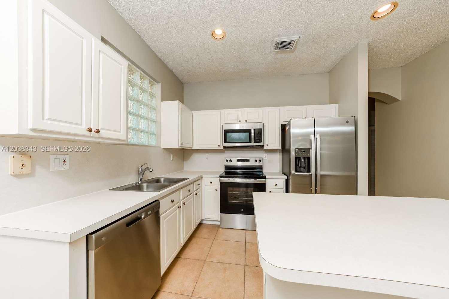 A kitchen features white cabinets, stainless steel appliances, a double sink, and tile flooring — BOYNTON BEACH, FL