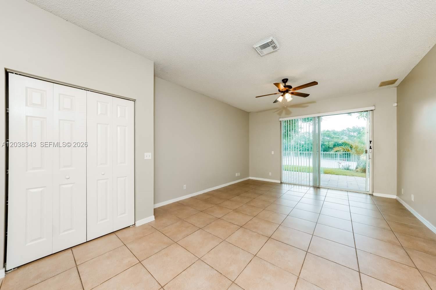 An empty room features beige tile flooring, a ceiling fan, and sliding glass patio doors — BOYNTON BEACH, FL