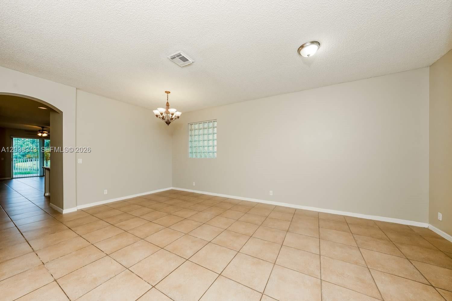 An empty room features beige tile flooring, a chandelier, and a glass block window — BOYNTON BEACH, FL