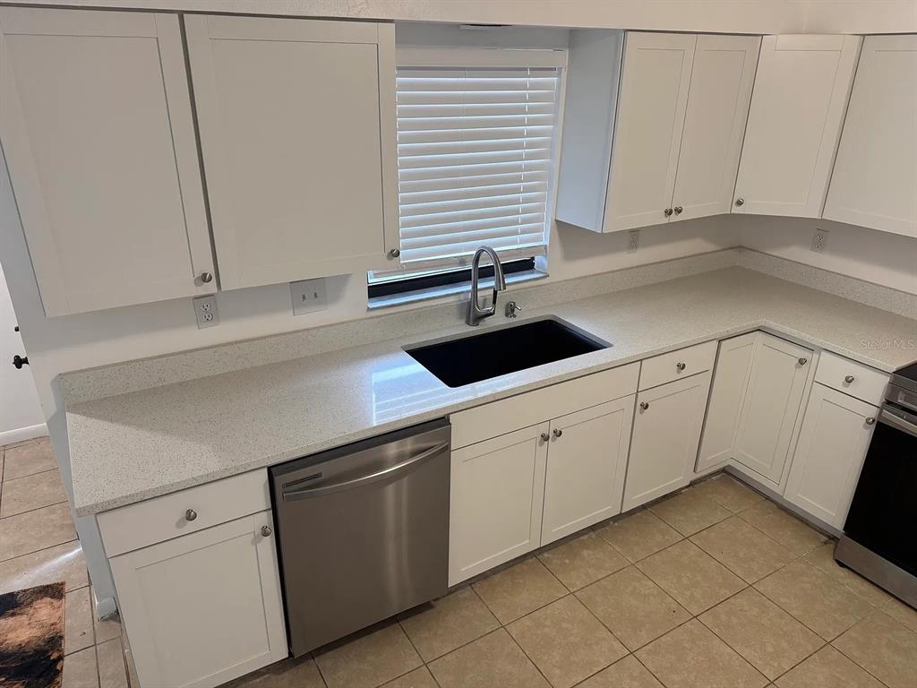 A kitchen features white cabinets, light speckled countertops, a black sink, and stainless steel appliances — 4845 16TH STREET, ZEPHYRHILLS, FL