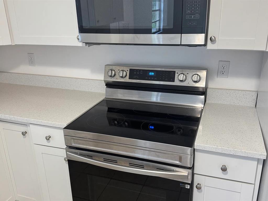 A kitchen features white cabinets, a stainless steel microwave, and a stainless steel electric range — 4845 16TH STREET, ZEPHYRHILLS, FL