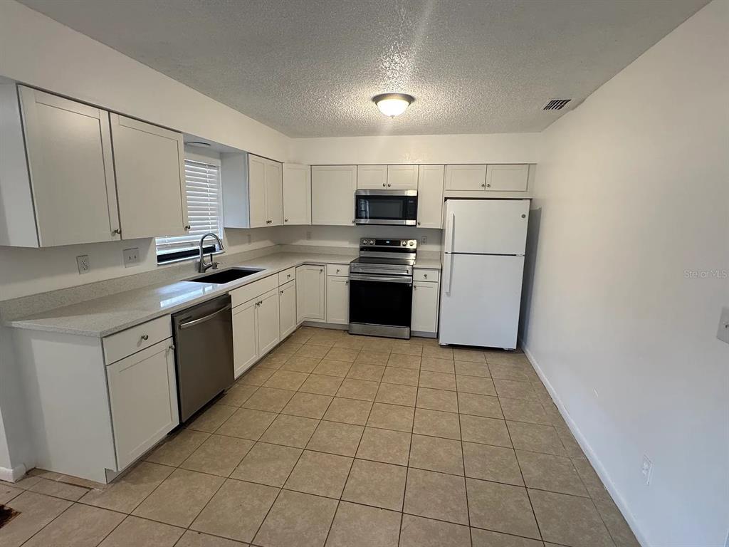 A kitchen with white cabinets, stainless steel appliances, light countertops, and beige tile flooring — 4845 16TH STREET, ZEPHYRHILLS, FL