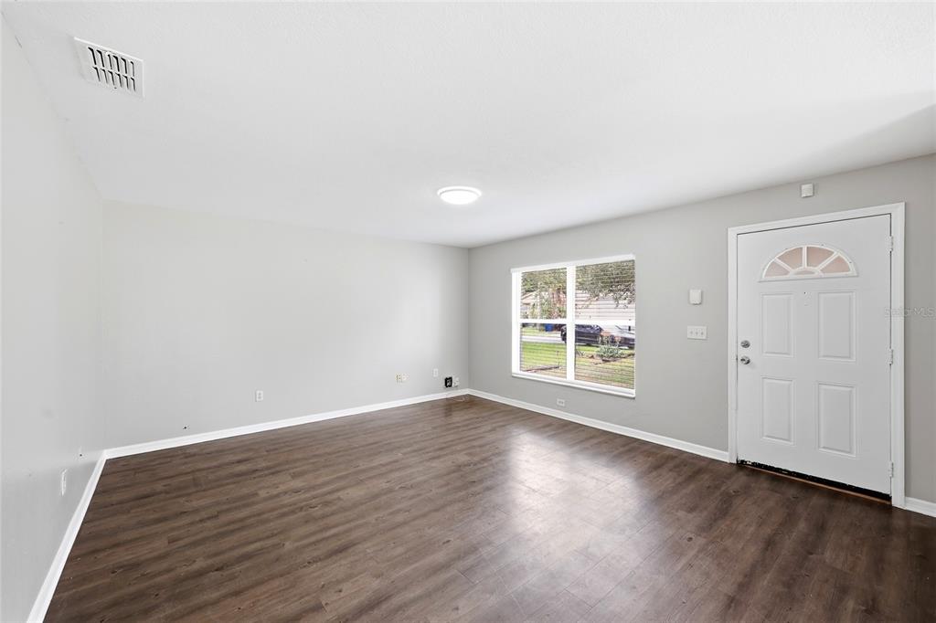 An empty room with light gray walls, dark wood-look flooring, a window, and a white door — 2214 E 19TH AVENUE, TAMPA, FL