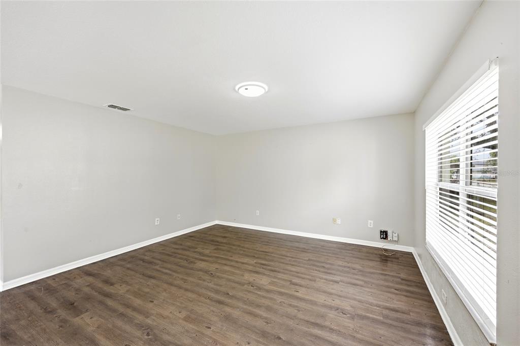 An empty room features light gray walls, dark wood-look flooring, and a large window with blinds — 2214 E 19TH AVENUE, TAMPA, FL