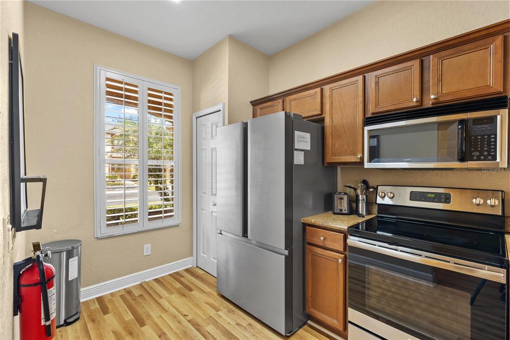 A kitchen features stainless steel appliances, wood cabinets, granite countertops, and a window with shutters — 3254 CALABRIA AVENUE UNIT 3254, DAVENPORT, FL