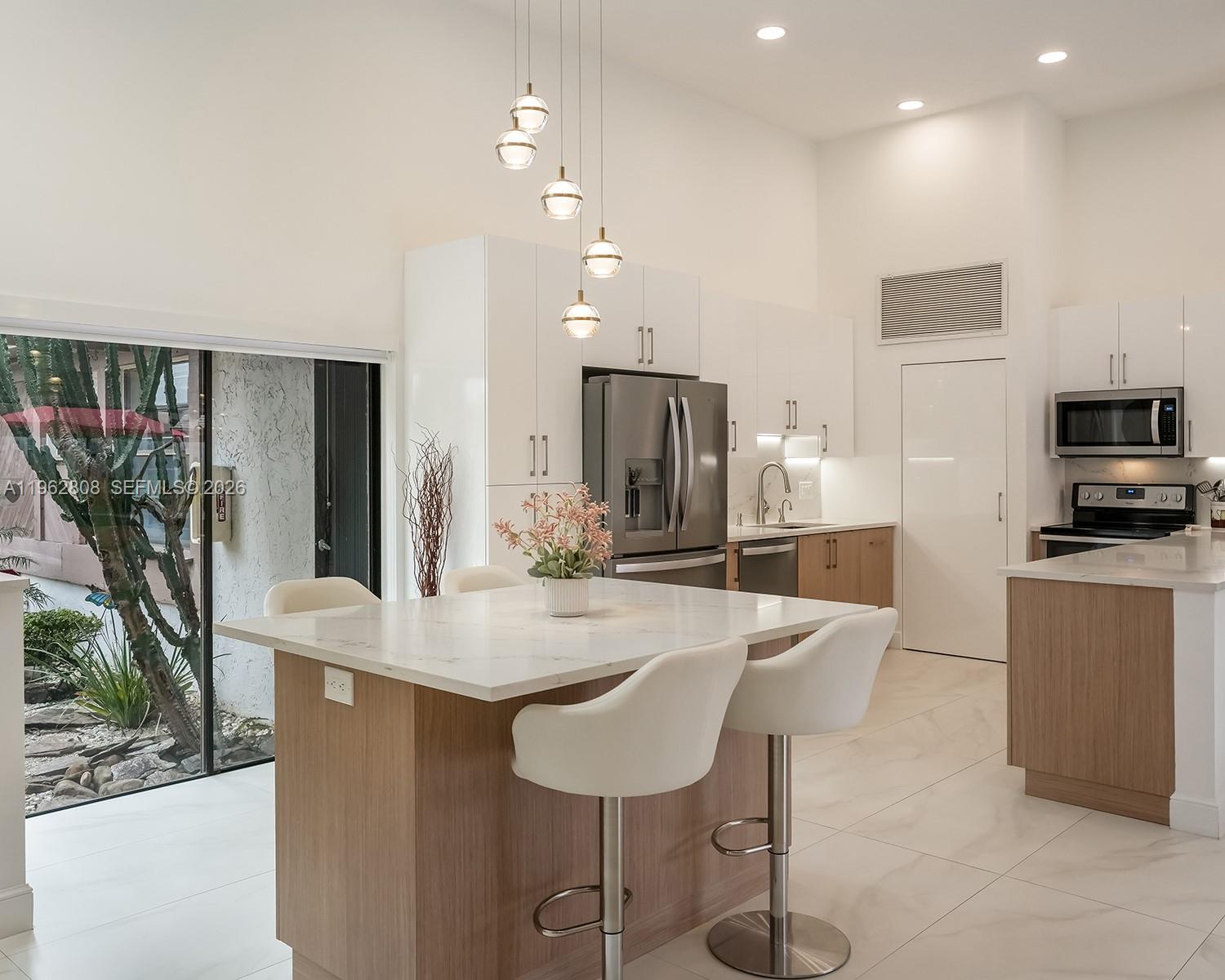A modern kitchen features a marble-topped island, white cabinetry, and a sliding glass door view — 413 Leslie Dr, Hallandale Beach FL 33009, HALLANDALE BEACH, FL
