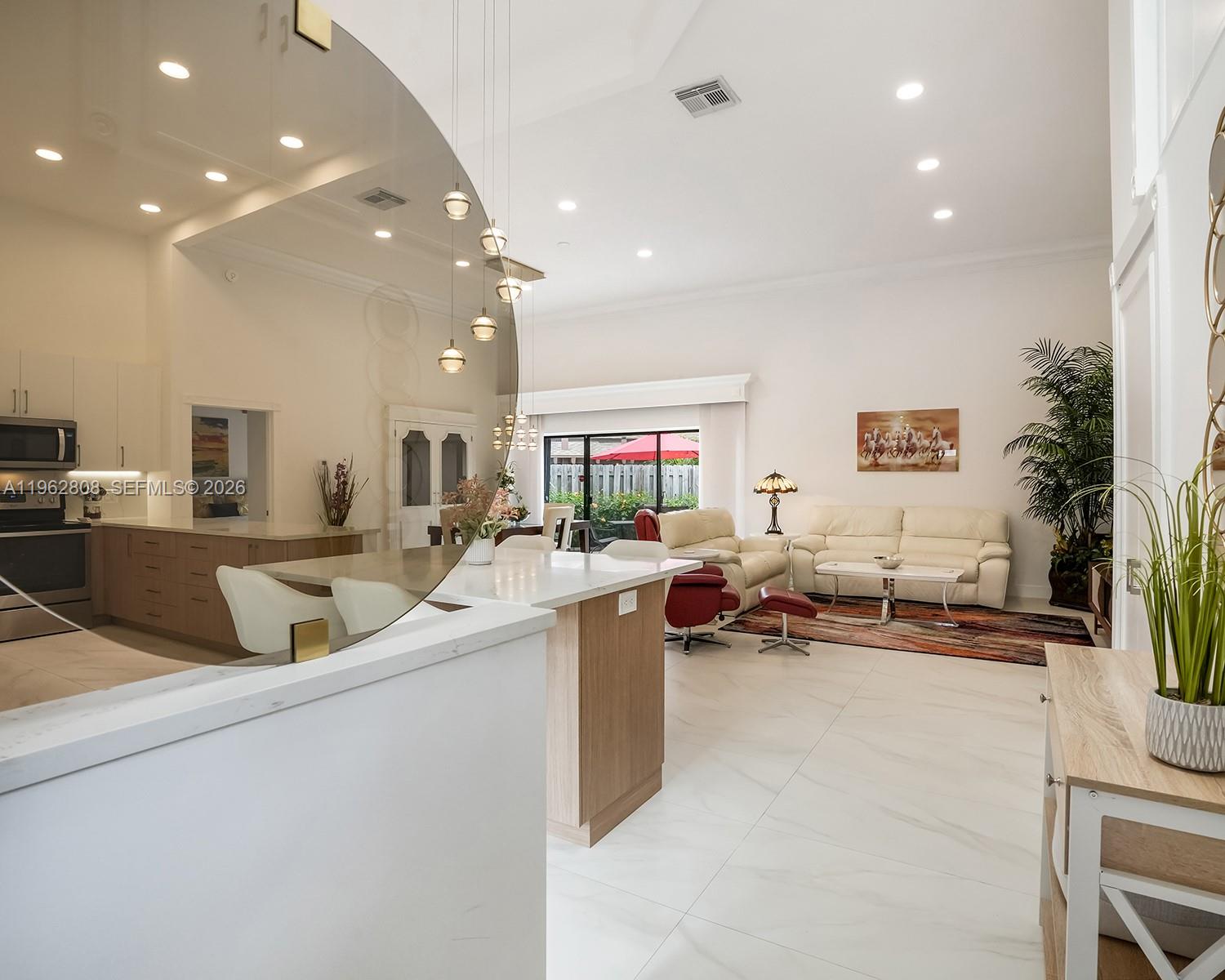 An open-concept living room and kitchen featuring white tile floors and modern light fixtures — 413 Leslie Dr, Hallandale Beach FL 33009, HALLANDALE BEACH, FL