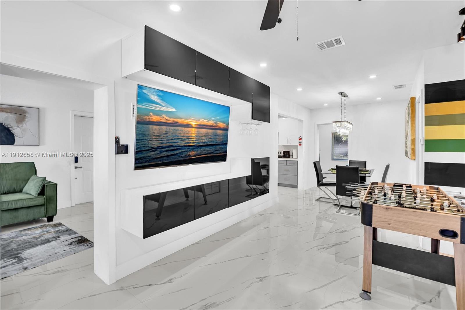 A modern living and dining area features a large wall-mounted television and marble-look flooring — 797 NW 35th St, Miami FL 33127, MIAMI, FL