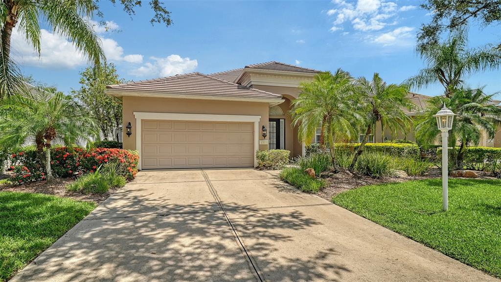 A single-story house with a beige stucco exterior, a two-car garage, and a concrete driveway — 6909 LENNOX PLACE, BRADENTON, FL