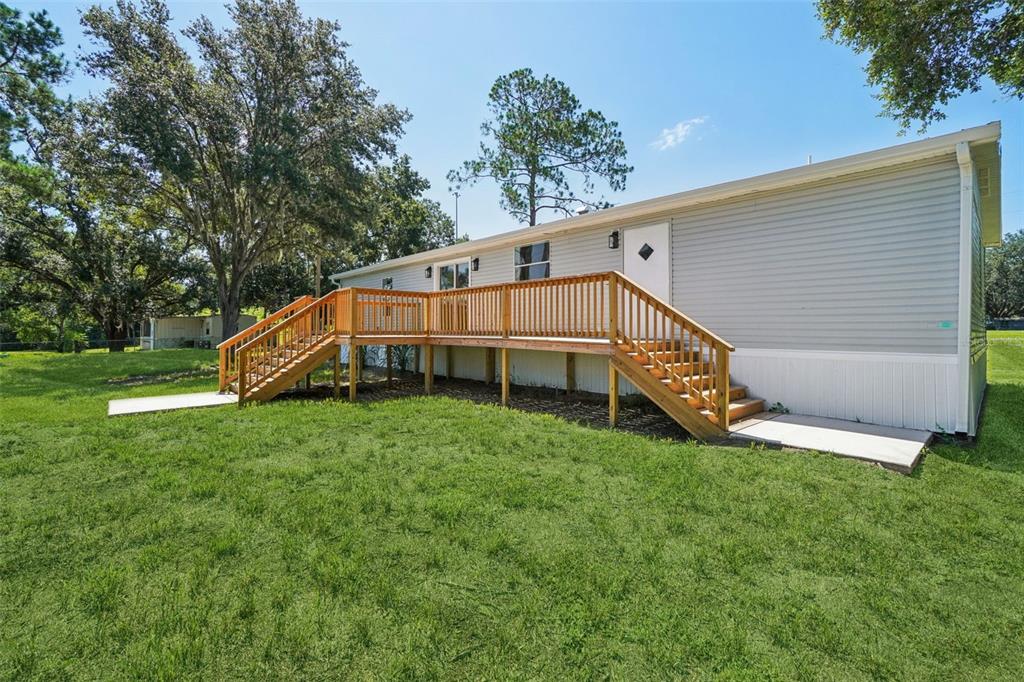A light gray manufactured home features a large wooden deck with stairs on both ends — 29417 KELLY DRIVE, WESLEY CHAPEL, FL