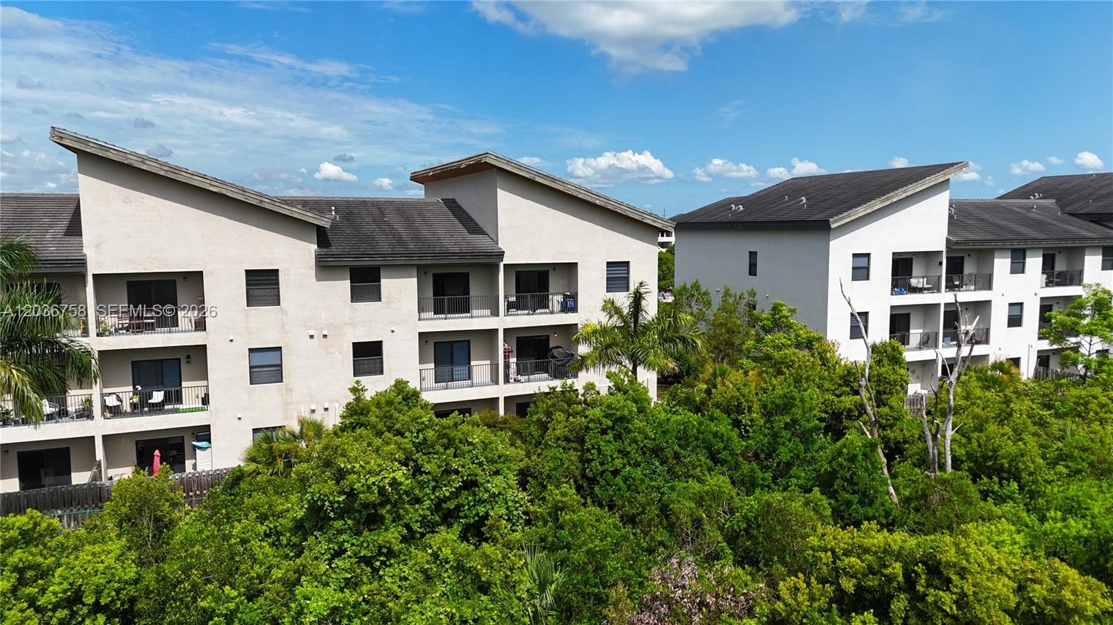 An exterior view of two multi-story apartment buildings surrounded by dense green trees — 7925 NW 104th Ave # 21, Doral FL 33178, DORAL, FL