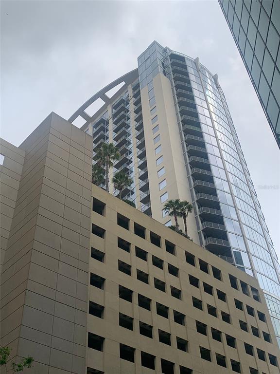 A tall, modern high-rise building with a parking garage base and palm trees on terraces — 155 S COURT AVENUE UNIT 1407, ORLANDO, FL