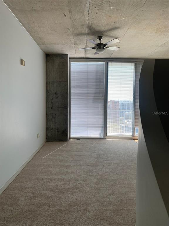 An empty room with carpeted floors, a concrete ceiling, and a large window with blinds — 155 S COURT AVENUE UNIT 1407, ORLANDO, FL