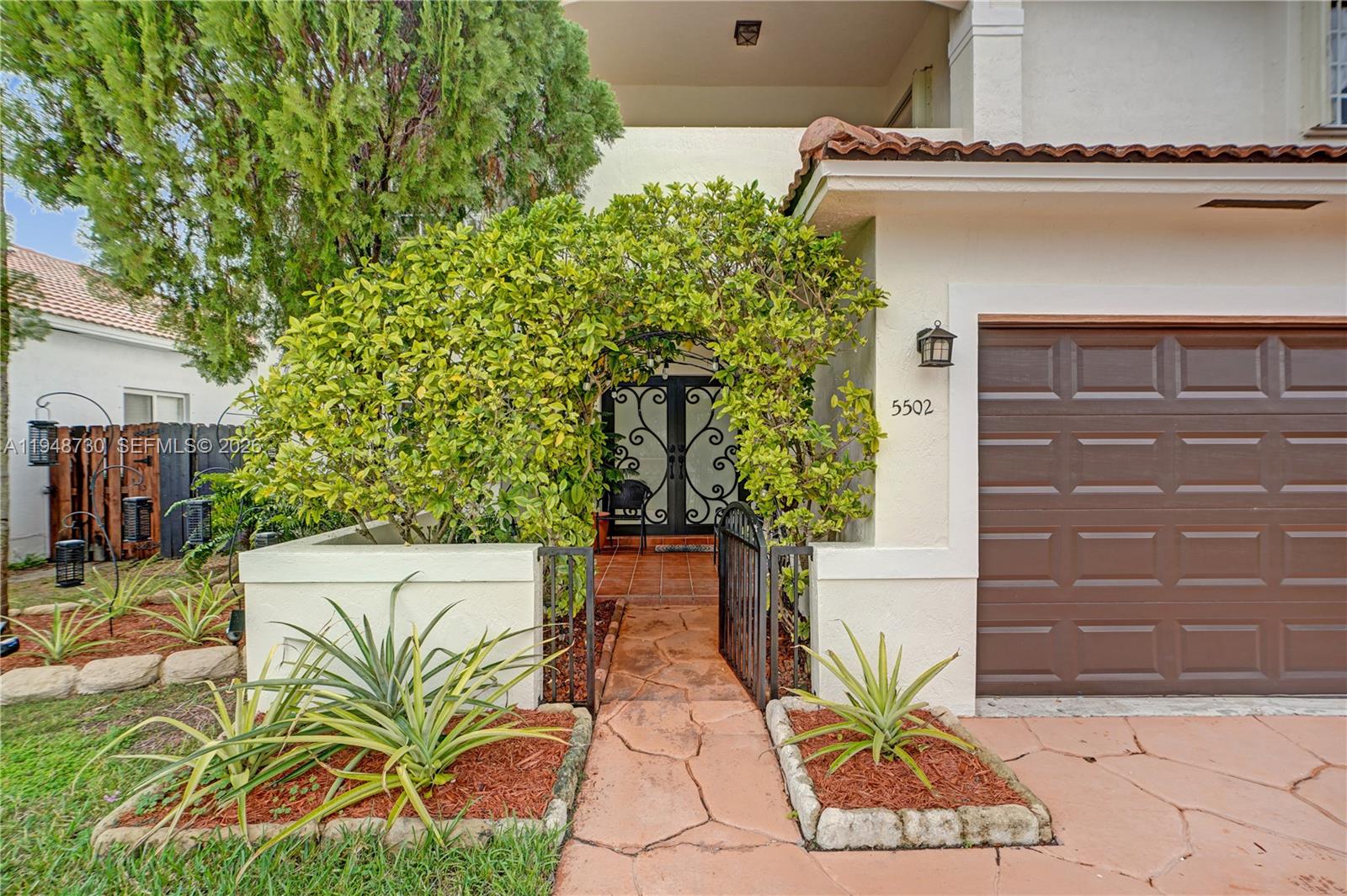 A stone walkway leads through a lush green archway to the front entrance of a house — 5502 SW 162nd Pl, Miami FL 33185, MIAMI, FL