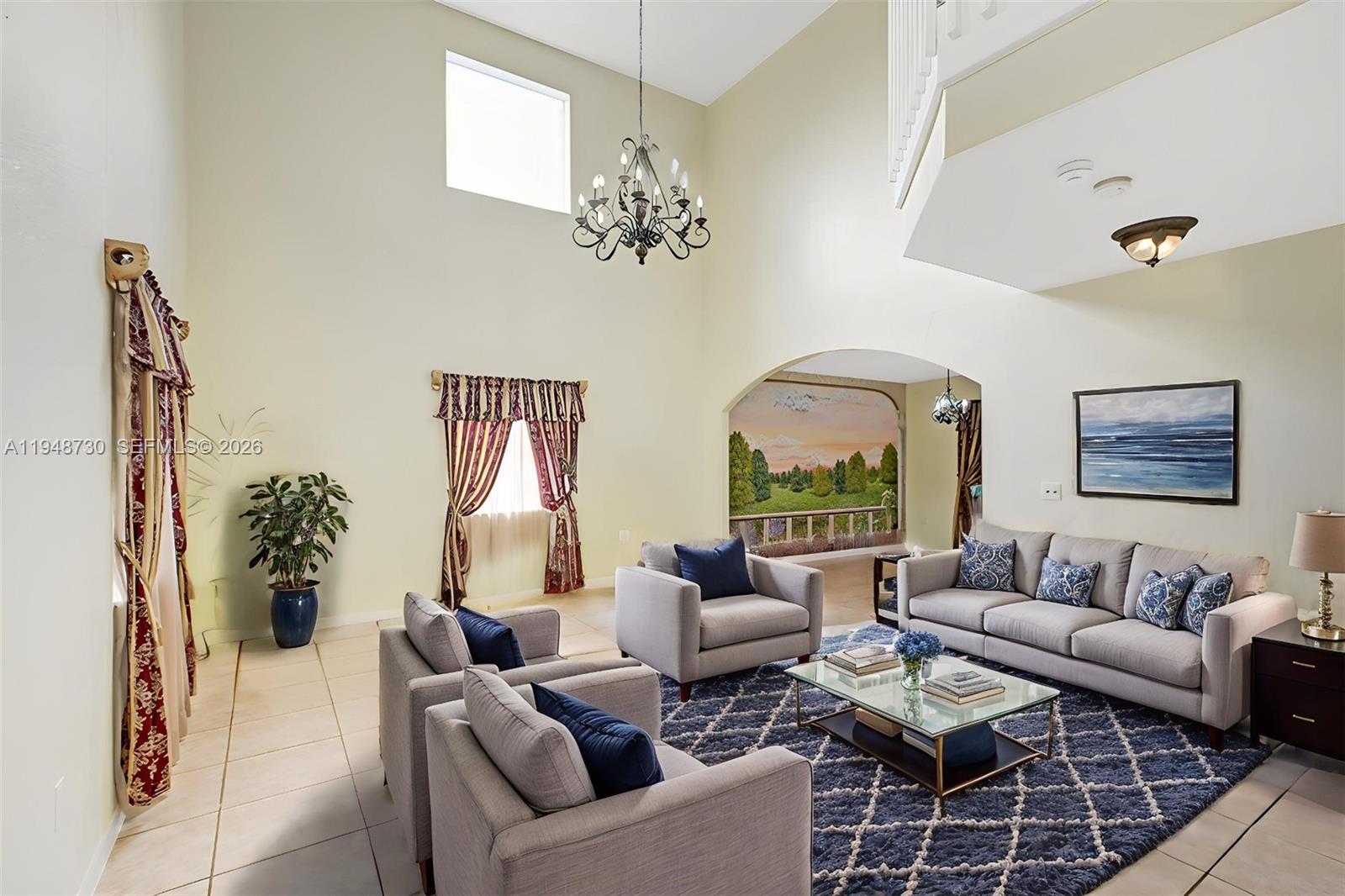 A living room features high ceilings, a chandelier, a mural, and gray upholstered furniture — 5502 SW 162nd Pl, Miami FL 33185, MIAMI, FL