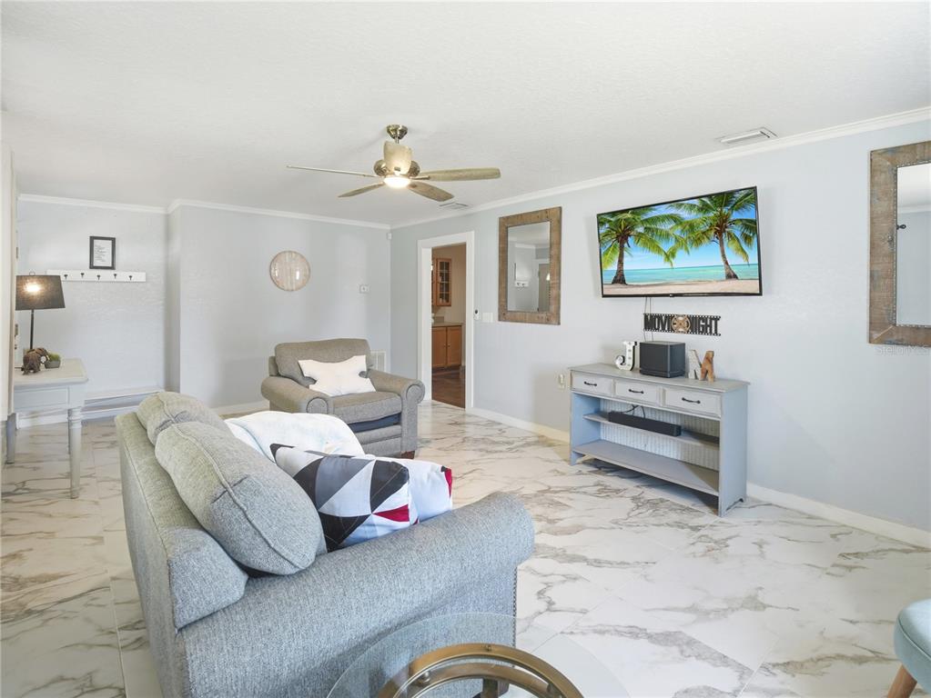 A living room features a gray sofa, an armchair, a television, and white marble flooring — 1423 LOUISIANA AVENUE, ST CLOUD, FL