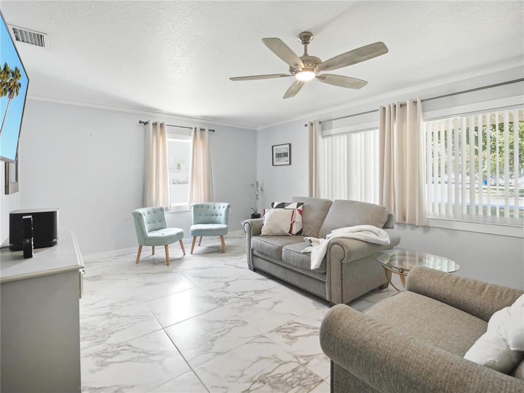 A living room features light gray walls, white marble-look tile floors, and a ceiling fan — 1423 LOUISIANA AVENUE, ST CLOUD, FL